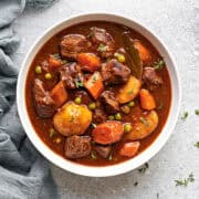 A white bowl of instant pot beef stew meat and gravy with potatoes, carrots and peas.