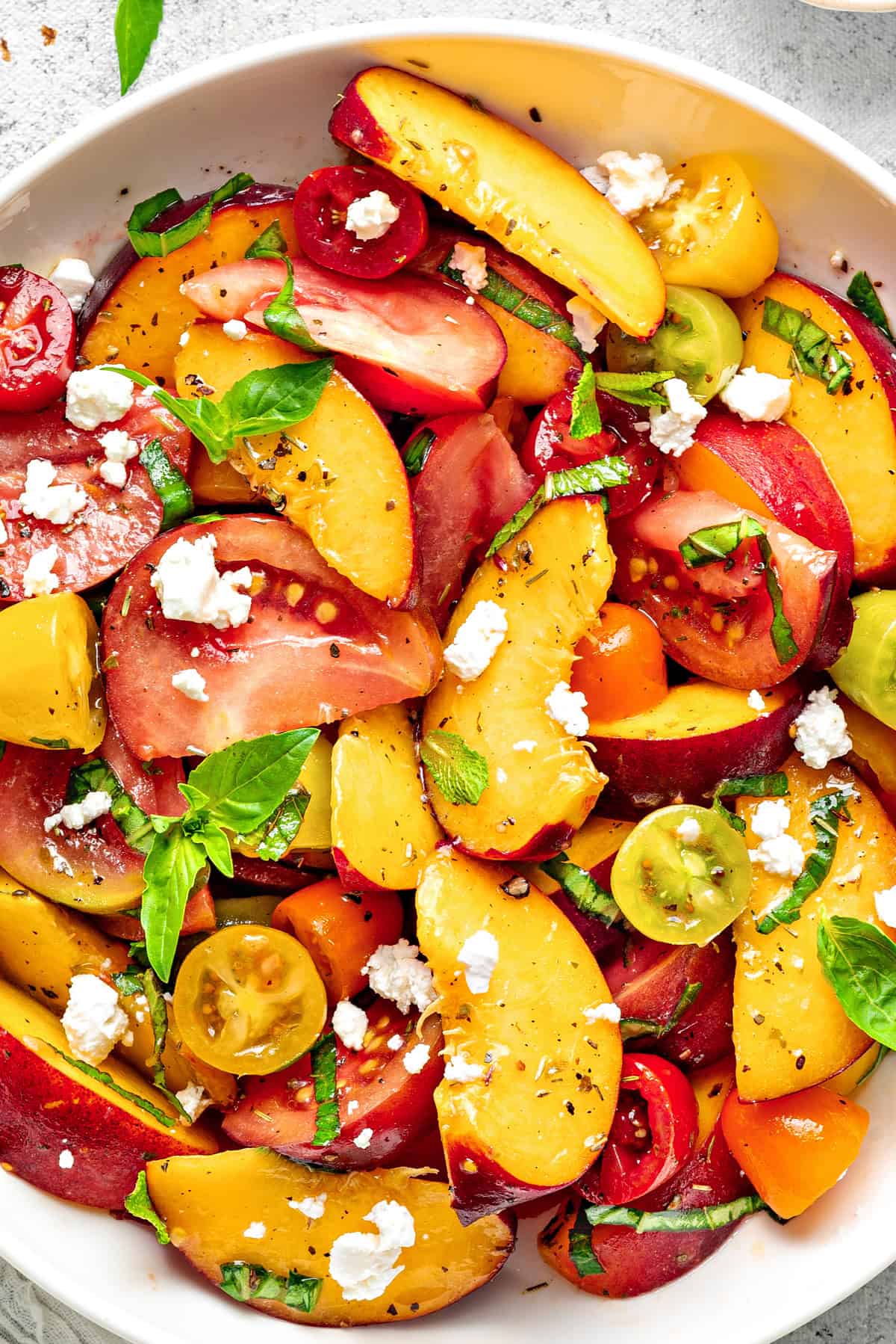 Peach and Tomato Salad in a bowl topped with feta, mint, and basil garnish, and ready to be served immediately.