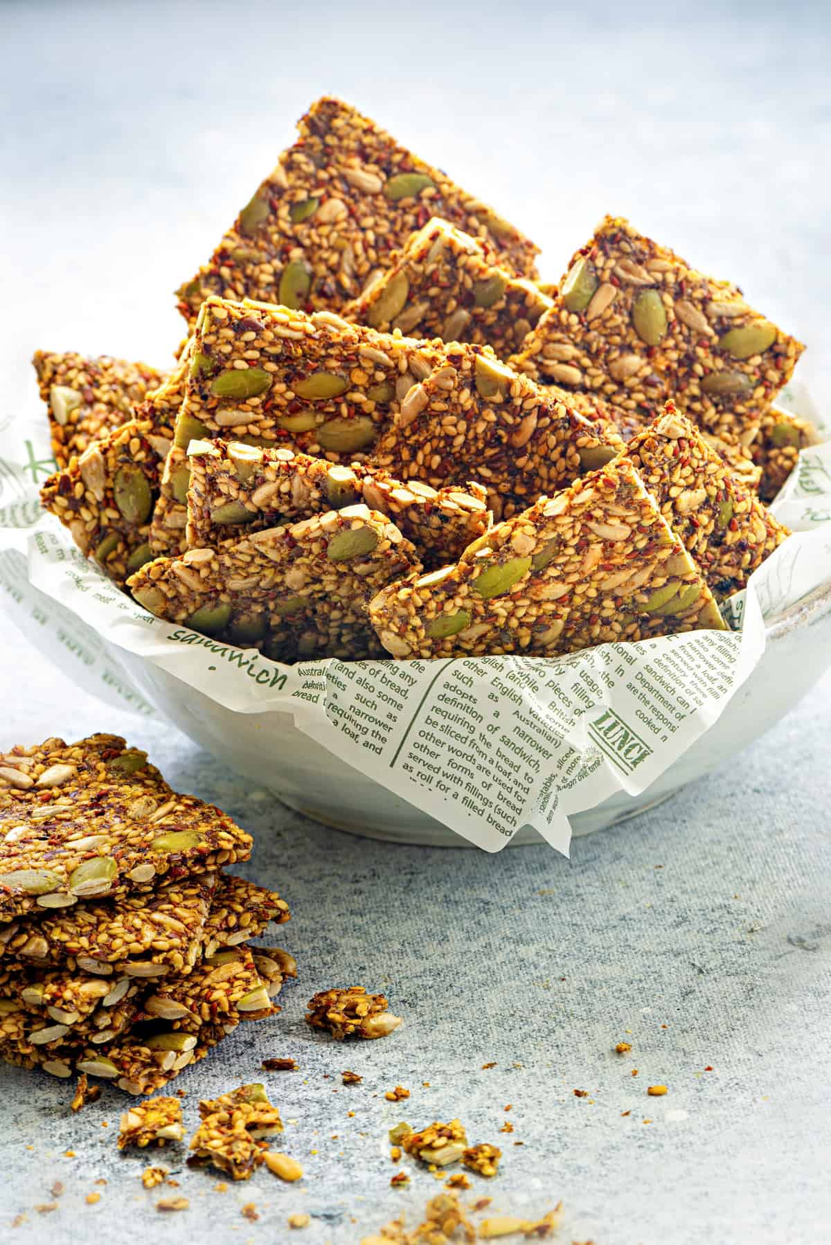 Close view of seed crackers stacked in a white ceramic bowl with parchment paper.