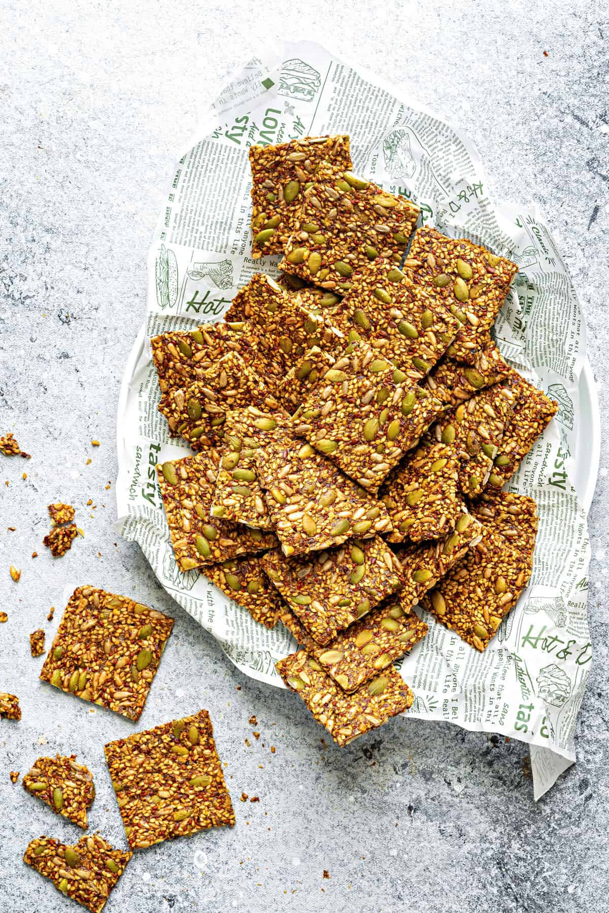 Top-down view of square seed crackers laying on a large platter on top of parchment paper.