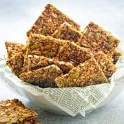 Close view of gluten-free mixed seed crackers stacked in a white ceramic bowl with parchment paper.