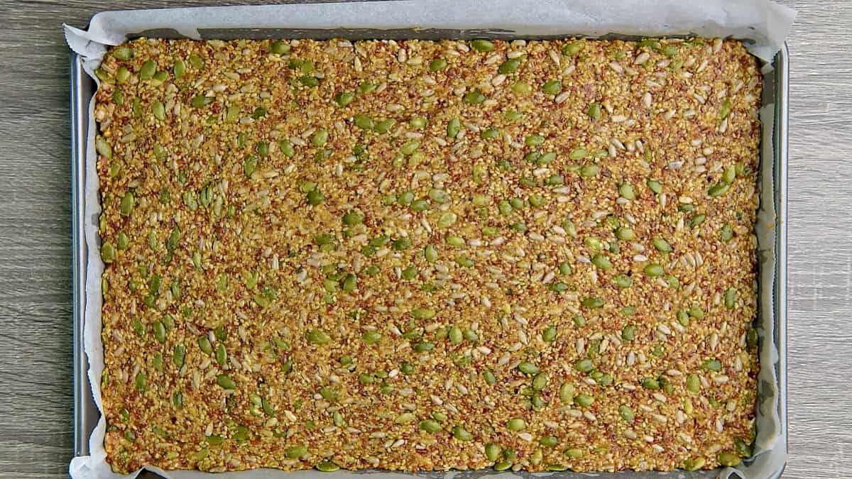 The seedy dough pressed down into a large baking sheet on top of parchment paper.