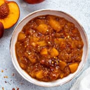 Top-down view of peach chutney in a serving bowl with red pepper flakes dusted on top.