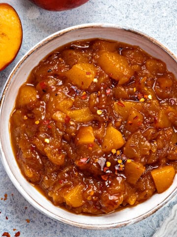 Top-down view of peach chutney in a serving bowl with red pepper flakes dusted on top.