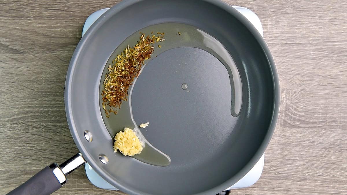 Oil, cumin, fennel, and garlic being heated in a pan.