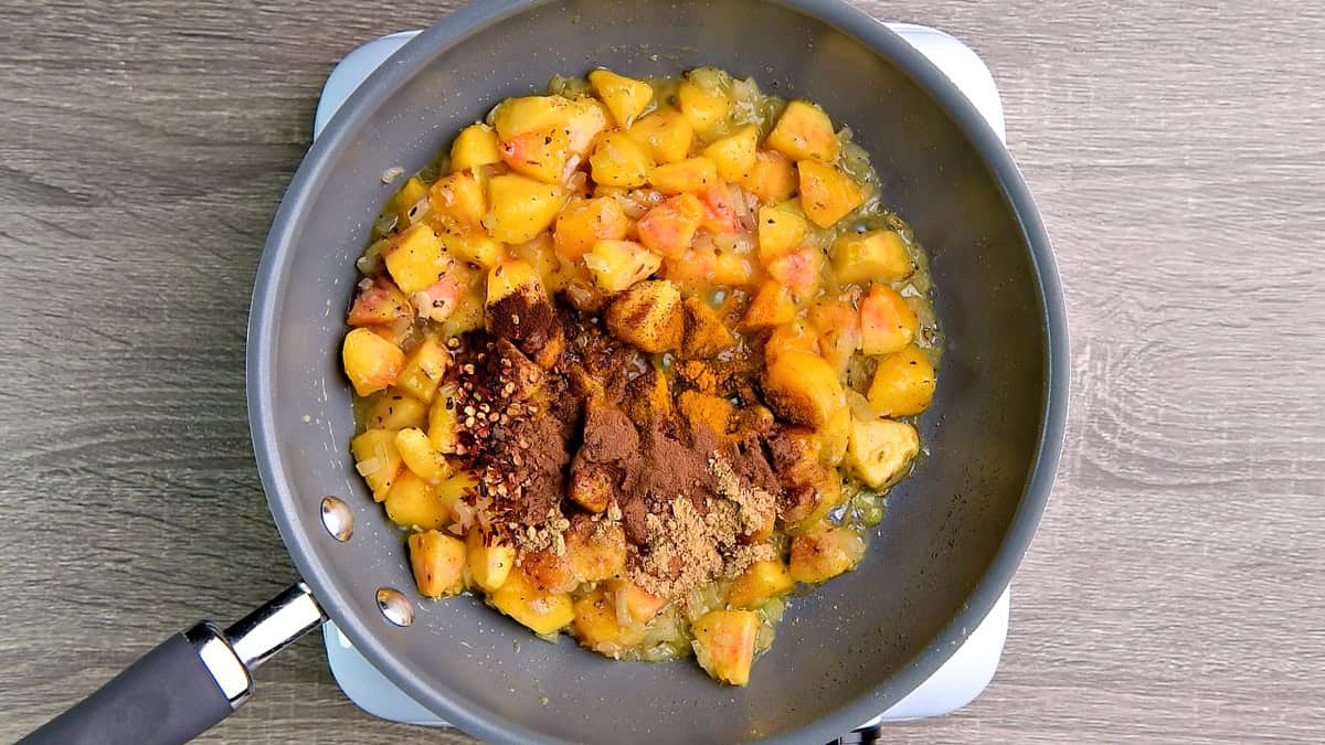 Spices added to the peach mixture in the pan include turmeric, red pepper flakes, clove powder, and more.