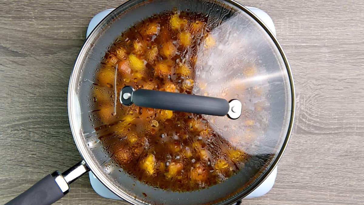 The pan with the chutney is being simmered on the stove with a lid on it for 10 minutes until the peaches are soft.