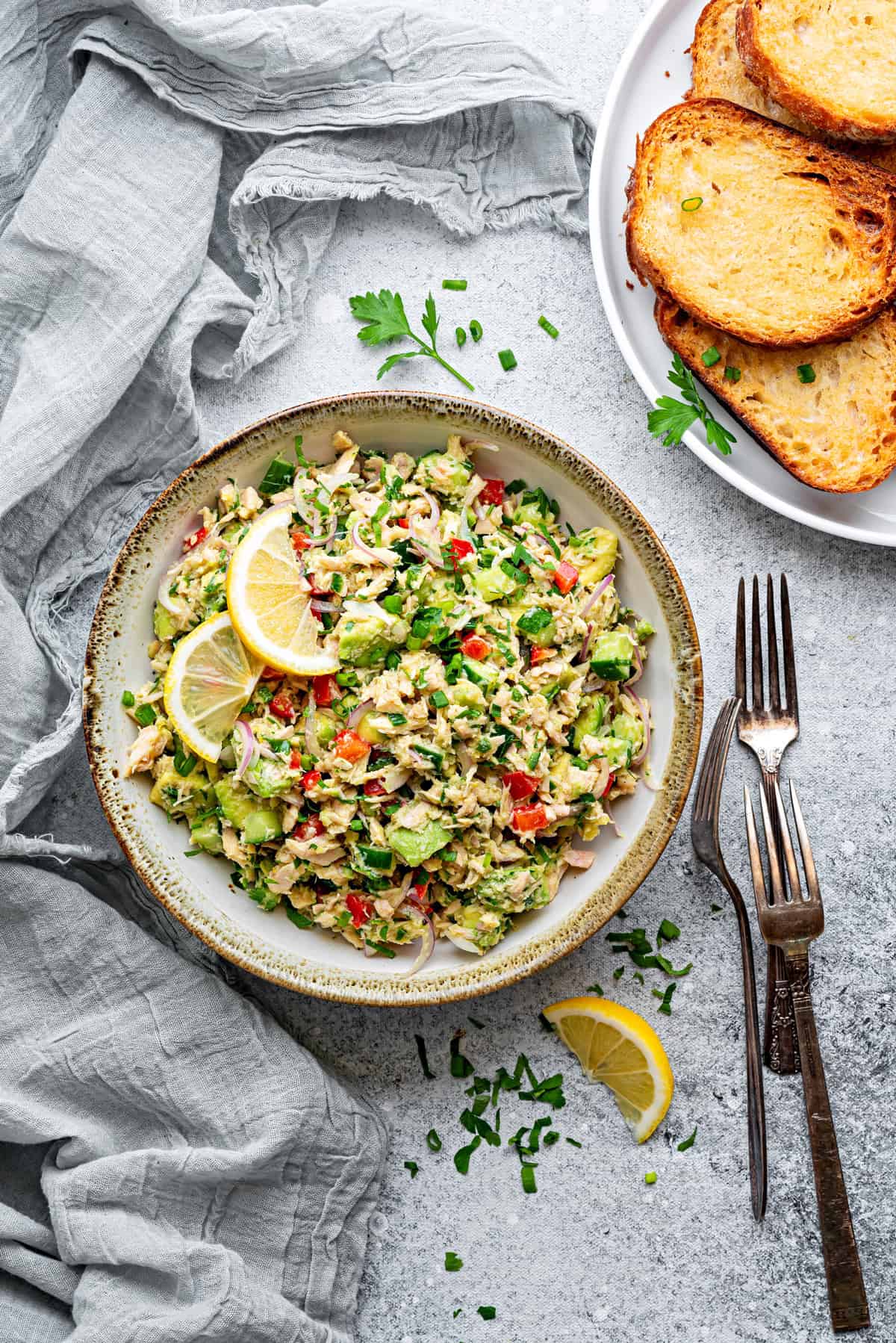 Top-down view of Avocado Tuna Salad with toasted bread and lemons ready to be served.