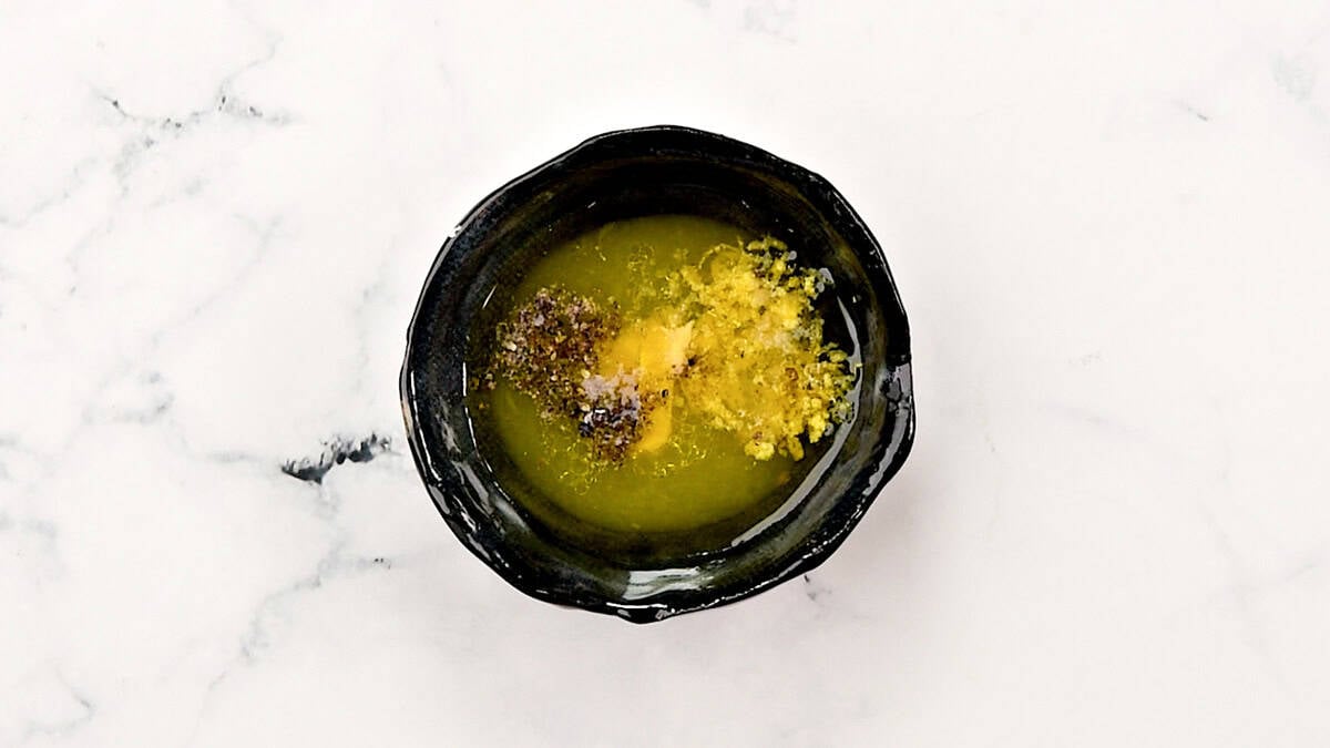 A small bowl containing the dressing for the tuna salad that has EVOO, lemon juice, Dijon mustard and seasoning.