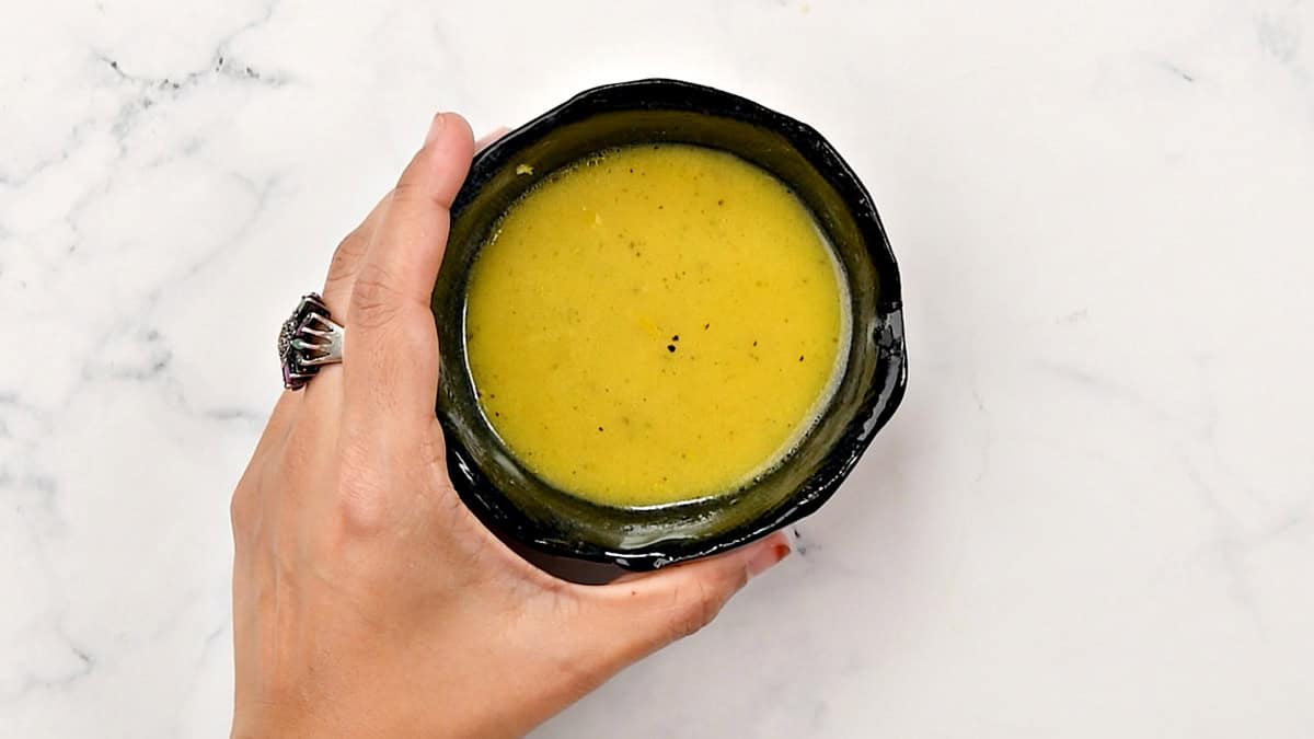 A hand holding a small bowl with dressing ingredients that have been mixed well.