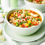 Side view of tomato macaroni soup with vegetables in a bowl.
