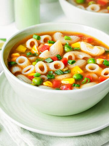 Side view of tomato macaroni soup with vegetables in a bowl.