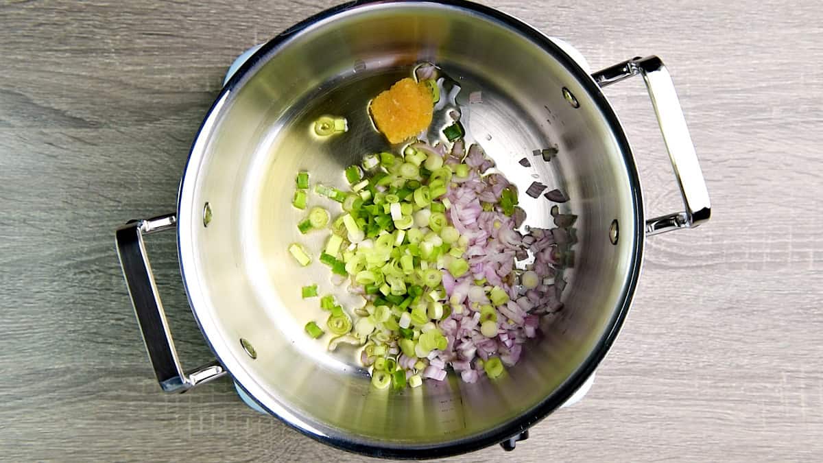 Chopped shallot, sliced scallions, and minced garlic sautéing in oil in a pot.