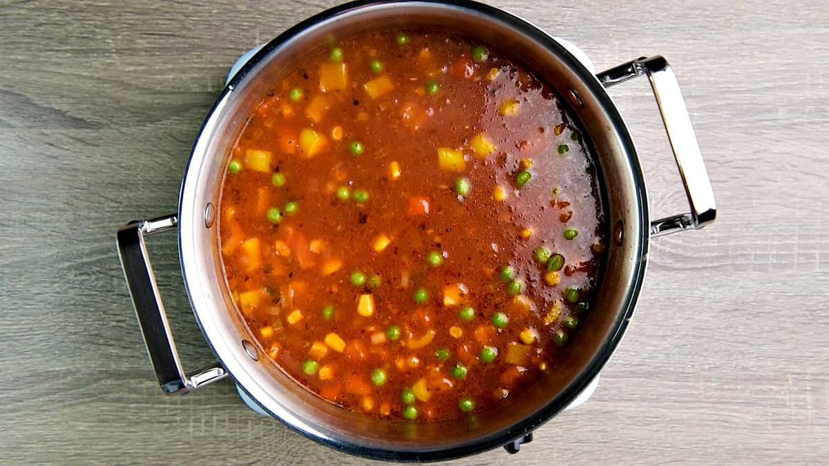 Frozen peas, corn, bell peppers, and macaroni added to the pot and simmered until the pasta is cooked yet still firm.