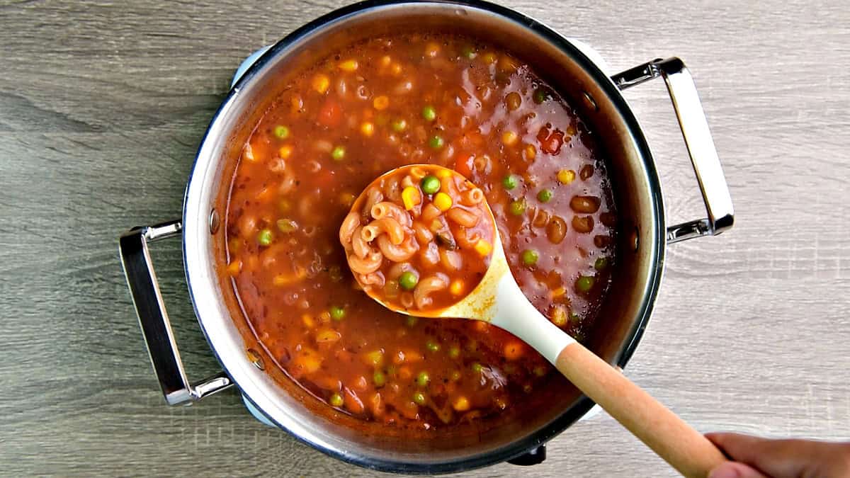 A ready-to-eat ladle of tomato macaroni soup with veggies.