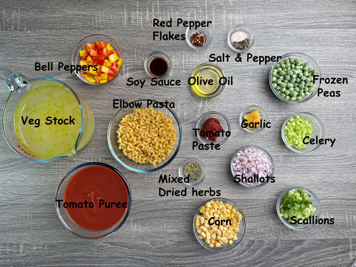 Top-down view of ingredients for soup recipe with veggies that include macaroni, corn, mixed herbs, scallions, and tomato puree.